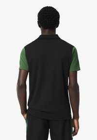 Polo nero con maniche corte verdi, caratterizzato da una texture liscia e un design con colletto classico. Vista posteriore che mette in evidenza il contrasto dei colori.
