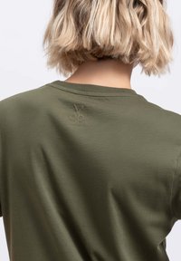 Olijfgroen T-shirt met een zachte textuur en een klein, reliëf schaarlogo op de bovenkant van de rug. Klassiek ontwerp met ronde hals.