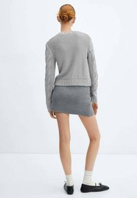 Szary sweter wykonany na drutach z kablowymi rękawami, w zestawieniu z szarym mini szortami. Modelka nosi kremowe skarpetki i czarne baleriny.