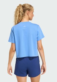 Afskåret blå t-shirt lavet af blødt stof, har korte ærmer, rund halsudskæring og et logo på ryggen. Bæres med marineblå shorts.