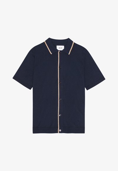 T-paita lyhyellä hihalla, tummansininen, valmistettu pehmeästä kankaasta, jossa on vaaleanruskea kaulus ja nappilista. Ribbattu helma.