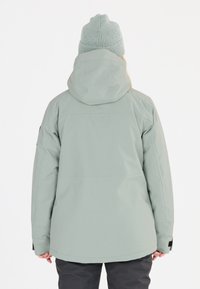 Ljusgrön vattentät jacka med huva, med en texturerad yta och justerbara ärmar, tillsammans med en matchande stickad mössa.