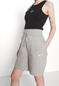 Černý bezrukávový top s zeleným logem Nike, spárovaný se šedými sportovními šortkami s tkaničkou a bílým logem swoosh Nike.
