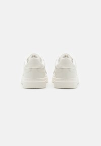 Hvite lær sneakers med avrundte bakstykk, jevn tekstur og flate gummisåler. Sømdetaljer langs hælen og sidene.