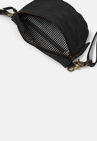 Black leather crossbody bag with brass hardware, zipper open to show black and white striped fabric lining and inner zip pocket.