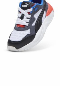 Sneakers Puma con tomaia in rete bianca, accenti neri e grigi, sezione centrale rossa, linguetta imbottita e suola in gomma. I lacci sono bianchi.
