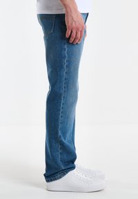 Vaqueros de mezclilla azul claro con un ajuste de pierna recta, que presentan un ligero desvanecimiento y un diseño estándar de cinco bolsillos. Llevados con zapatillas blancas.