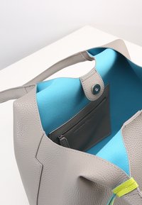 Szara skórzana torba tote z teksturowaną powierzchnią, niebieską tkaniną wewnętrzną i zapięciem na zatrzask. Ma kieszeń na zamek błyskawiczny i neonowe akcenty.