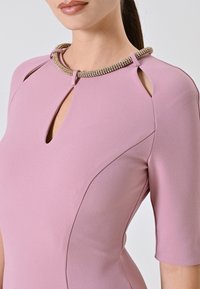 Abito rosa con scollatura a chiave, maniche corte e colletto decorativo con perline. Tessuto liscio con dettagli di cuciture curve.