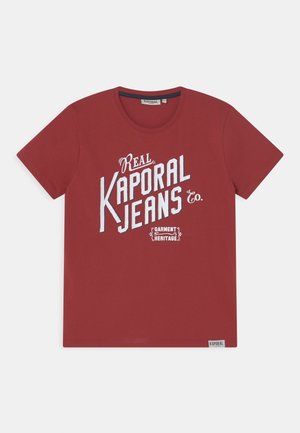 Rotes T-Shirt mit kurzen Ärmeln und weißem Schriftzug "Real Kaporal Jeans Co." sowie kleinem "Garment Heritage"-Logo, zentral auf der Vorderseite platziert.