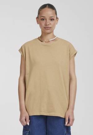 T-shirt beige, surdimensionné avec des manches courtes retroussées. Tissu en coton doux, encolure ronde. Porté avec un bas en denim et un collier superposé.