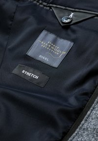 Black fabric with a satin finish displays tags reading "FINest Silk Wool Selection" and "DIGEL." The "STRETCH" tag is white on black.