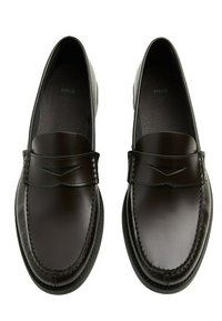 Kaksiosaiset tummanruskeat nahkalöysärit, joissa on ommeltu yksityiskohtia, pyöristetty kärki ja helposti jalkaan sujautettava malli, nähtynä ylhäältäpäin.