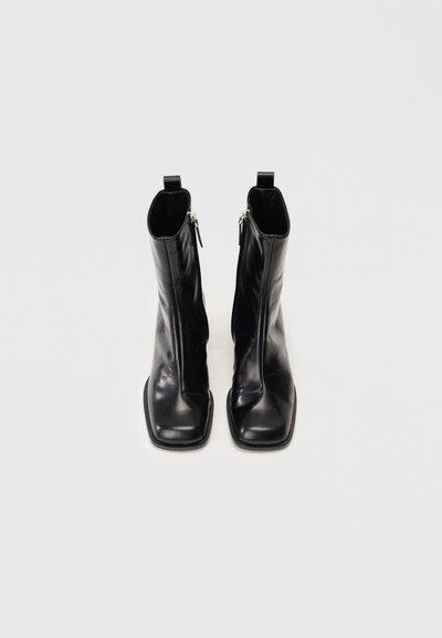 Μαύρες δερμάτινες ανδρικές μπότας αστραγάλου με τετράγωνη μύτη, πλάγιες φερμουάρ και υφασμάτινη σόλα από καουτσούκ. Διαθέτουν λεία υφή και μίνιμαλ σχεδίαση.