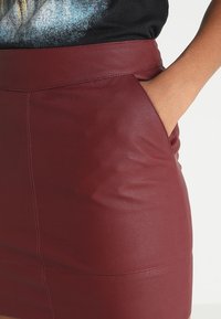 Burgundy fusk läder mini kjol med en slät yta, med en åtsittande midjeband och sidofickdetalj.