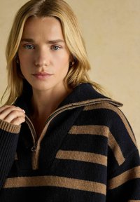 Zippter Pullover mit dunkelblauen und beigen horizontalen Streifen, gerippten Bündchen und einem strukturierten Strickdesign. Weiche, lässige Passform.