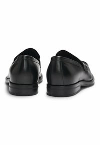 Black leather loafers featuring a smooth texture, rounded shape, low heel, and subtle stitching details on the back.