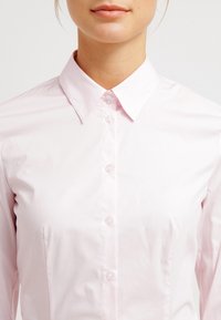 Camicia collerata rosa chiaro con bottoni frontali, maniche lunghe e una struttura liscia. Presenta un design classico con una silhouette aderente.