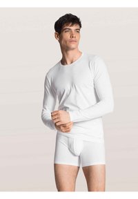 Camicia bianca a maniche lunghe con scollo rotondo e boxer bianchi. Entrambi realizzati in tessuto morbido, dal design aderente, che mettono in risalto uno stile minimalista.