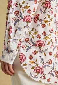 Valge särk, millel on mitmevärviline lilleline print punase, roosa, kollase ja sinisega. Omaduseks on kaardus alus ja nööpidega mansetid. Pehme puuvilla tekstuur.