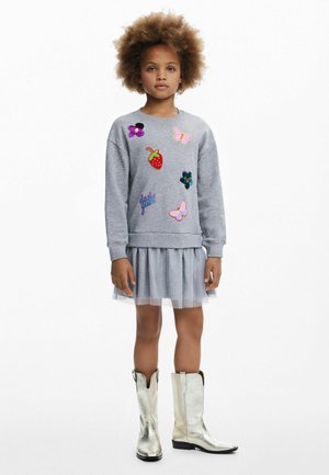 Grijze sweatshirt met kleurrijke geborduurde patches, gelaagde grijze tule jurk en glanzende zilveren cowboylaarzen. Eenvoudig en trendy ontwerp.