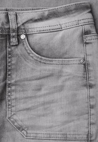 Šedá džínová tkanina má přední kapsu s prošitým obrysem a kovovým knoflíkem. Hladká textura s jemnými stínovacími detaily.