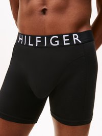 Fekete boxer alsónadrág széles gumipánttal, amelyen a "HILFIGER" fehér logó található. Simára szőtt anyag, szoros illeszkedéssel és látható minták nélkül.