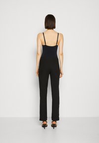 Černé kalhoty s vysokým pasem a námořnický bodysuit s tenkými ramínky, hladká textura a přiléhavý design, viděné zespodu. Viditelné podpatky.