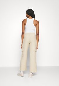 Beige cargo bukser med brede ben og to sidelommer, parret med en tætsiddende hvid tanktop. Stoffet har en tekstureret overflade.