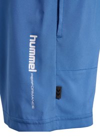 Niebieskie spodenki sportowe z białym logo „hummel PERFORMANCE” i małą czarną metką z symbolami w kształcie jodełki blisko brzegu.