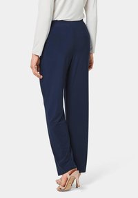 Marineblauwe wijde broek gemaakt van zachte stof, met een elastische tailleband en een gladde textuur. Draag het met beige hoge hakken.