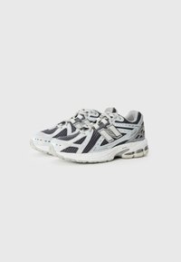 Chaussures de course avec une tige en mesh blanche et marine, des accents gris et un col rembourré. Présente un design à lacets et une semelle rembourrée avec une unité d'air visible.