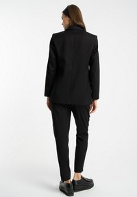 Czarny żakiet i dopasowany komplet spodni. Żakiet ma wycięty kołnierz i zdefiniowany krój. Teksturowana tkanina o minimalistycznym designie. Płaskie buty.