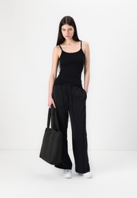 Svart tank topp, løse svarte bukser og en svart handlenett. Hvite joggesko. Glatt stoff med et enkelt design, uten synlige mønstre eller detaljer.