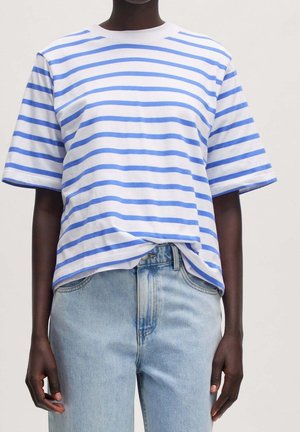 Osoba ubrana w biały krótki rękaw z niebieskimi poziomymi paskami oraz jasnoniebieskie, wysokowtalne jeansy na jednolitym tle.