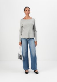 Gray long-sleeve top with a rounded neckline, paired with wide-leg light blue jeans. Holding a metallic silver handbag. Black pointed shoes.