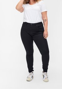 Jeans negros de talle alto con un corte ajustado, combinados con una camiseta de cuello en V de manga corta blanca y zapatillas blancas con detalles en negro.