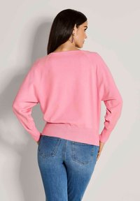 Rosa Strickpullover mit lockerer Passform, gerippten Bündchen und Saum. Kombiniert mit hellblauen Jeans mit Gesäßtaschen. Einfache und weiche Textur.