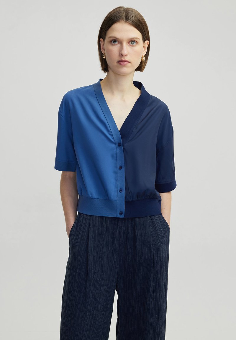 Kurzärmelige Bluse mit einem Farbblockdesign in unterschiedlichen Blautönen, glatter Satintextur, V-Ausschnitt und Knopfverschluss.