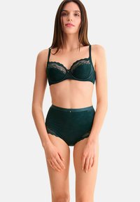 Soutien-gorge en dentelle vert foncé avec bonnets rembourrés, bords scallopés et bretelles ajustables. Culottes taille haute assorties avec des accents en dentelle et un tissu texturé.
