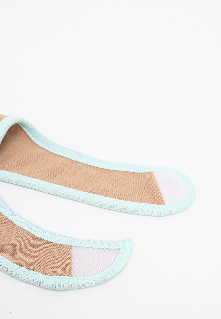 Chaussettes beiges invisibles avec des bordures bleu clair et des bords de capuchon blanc, posées à plat sur une surface blanche.