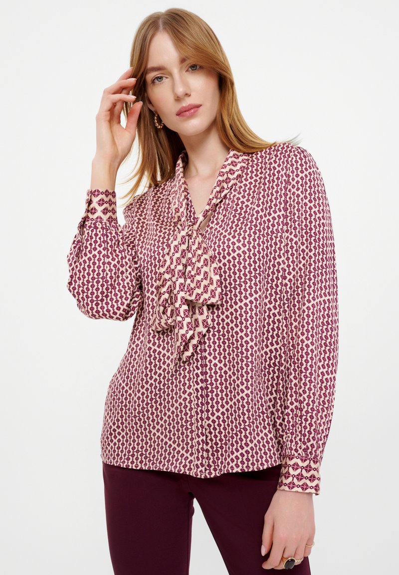 Vloeiende blouse in lichtroze met een bordeaux geometrisch patroon, met een striknek en knoopmanchetten. Zachte, gestructureerde stof.