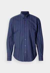 Tumesinine triiksärk pika varrukaga, millel on vertikaalsed triibud, nööbitav krae ja peen logo. Omab kõverat serva ja nöörihmadega kaunistusi.