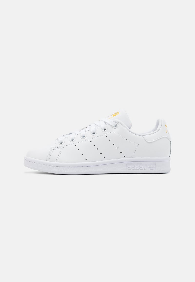 Hvite lær sneakers med lav profil, rund tå, snøring og perforerte sider. Har detalj med gult logo og gummisåle.