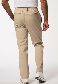 Pantaloni beige con vita elasticizzata, due tasche posteriori e gambe affusolate, realizzati in un tessuto liscio, abbinati a sneakers bianche.