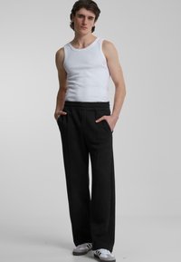 Black wide-leg trousers with a soft texture, featuring a stretchy waistband and side pockets, paired with a fitted white tank top.