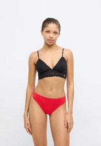 Bralette de encaje negro con bordes festoneados y tirantes finos, combinado con panties rojos festoneados, ambos con una textura suave.