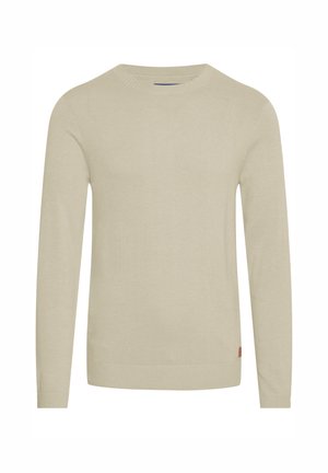 Pull en tricot beige à manches longues, col rond côtelé et ourlet. Texture douce avec une petite étiquette logo en bas à gauche.
