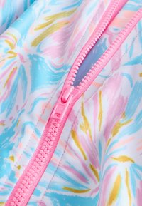 Pogled od blizu na rožnati zadrgo na tkanini z modrimi, rožnatimi in zlatimi abstraktnimi cvetličnimi vzorci, ki prikazuje zadrgane zobe in podrobnosti šivov.