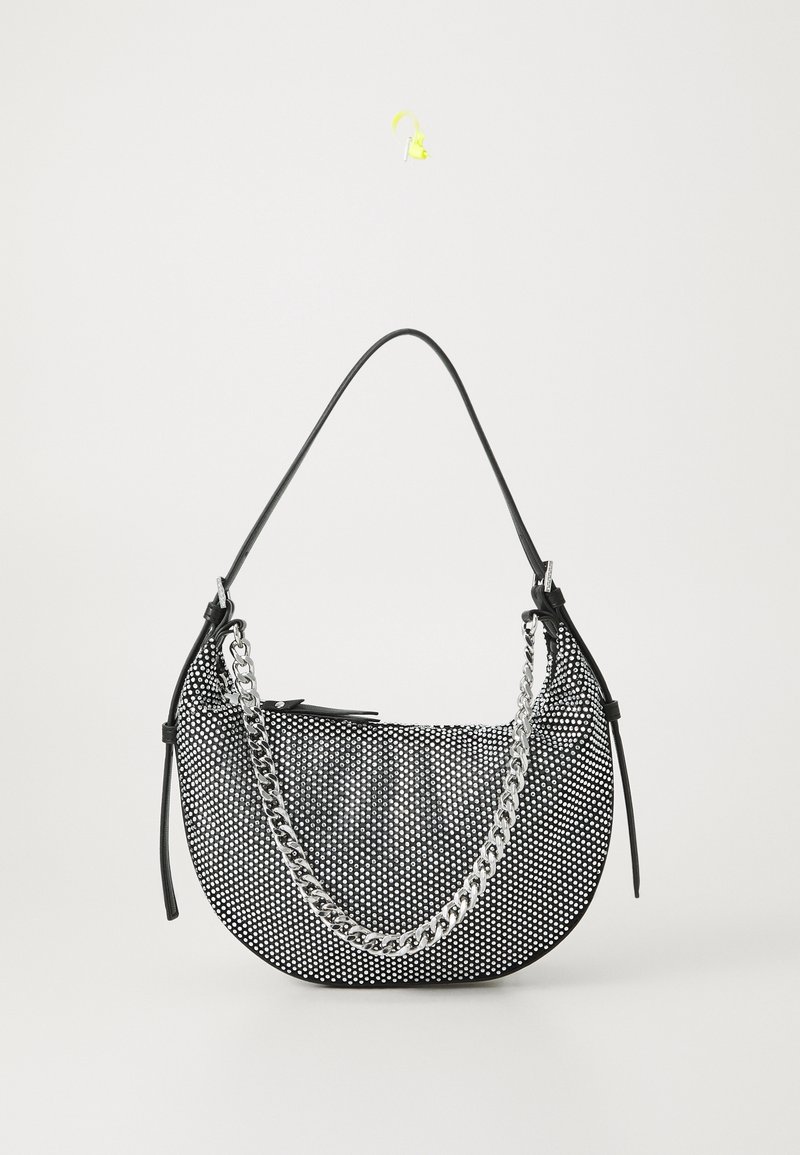 Sac à main croissant à pois blancs et noirs avec une bandoulière noire et un détail de chaîne argentée sur fond blanc.
